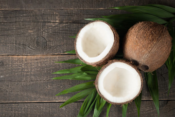 Ripe half cut coconut with green leaves on a wooden background.