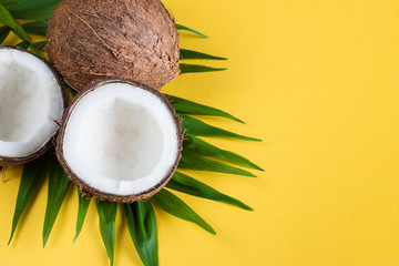 Ripe half cut coconut with green leaves on a yellow background.