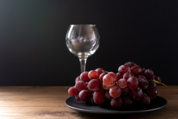 Bunch of ripe purple grapes in a bowl and a wine glass on a wooden background in the sun. Side view