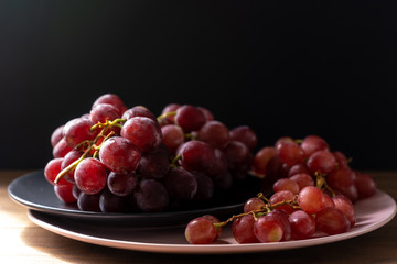 Bunches of ripe purple grapes on plates on a wooden table on a black background in the sun. Side view. Close-up