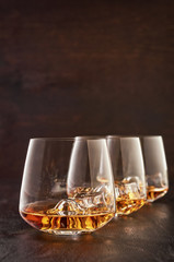 Three crystal glasses of whisky with ice on a wooden table.