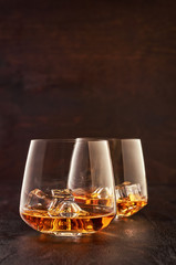 Two crystal glasses of whisky with ice on a wooden table.