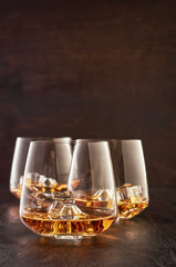 Three crystal glasses of whisky with ice on a wooden table.