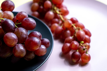 Bunches of ripe purple grapes on the pink plate and in a bowl on a yellow background in the sun. Close-up