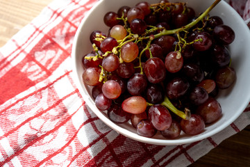 Bunch of ripe purple grapes in a white bowl on a wooden table in the sun. Side view. Close-up