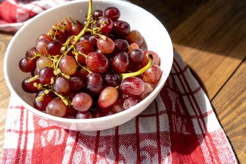Bunch of ripe purple grapes in a white bowl on a wooden table in the sun. Side view