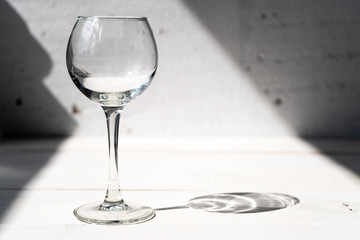 Glass wine glass on the left on a white table on a white background under the sun. 