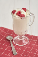 Glass with whipped cream and raspberries on a checkered napkin