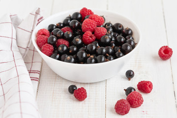 Fresh berries are in white bowl. nearby is napkin