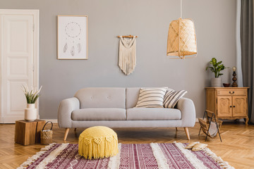 Stylish and design home interior of living room with gray sofa, wooden cube, commode, pillow, macrame, yellow pouf, rattan lamp, basket, plants and elegant accessories. Stylish home decor. Template. 