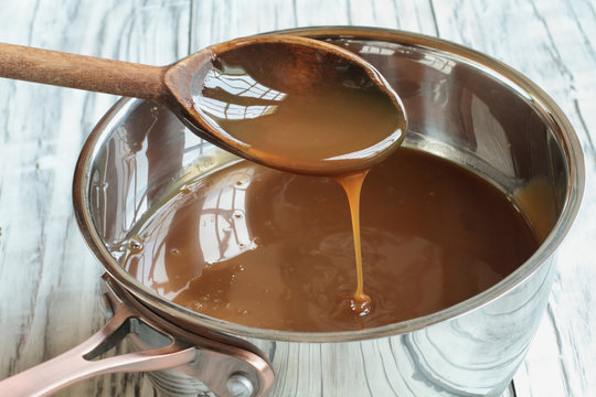 Wooden spoon dripping caramel sauce into a pan. Selective focus with blurred background.