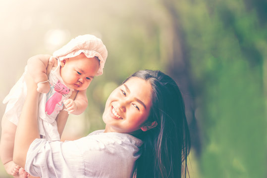 Young beautiful asian mother smiling and holding little baby girl playing in the park.