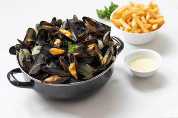 Belgian mussels with potato fries and sauce on white marble table