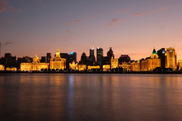 Beautiful sunset of The Bund in Shanghai. Golden illuminated western buildings on the bank of Huangpu River. Long exposure peaceful river. Wide angle