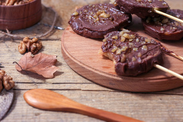 Slices of apples in chocolate, caramel glaze and walnuts on skewers on a wooden background