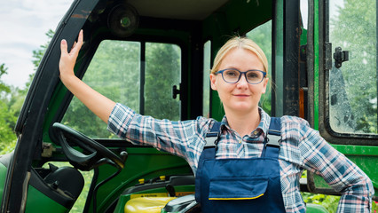 Portrait of a farmer woman. Standing near his tractor, looking at the camera