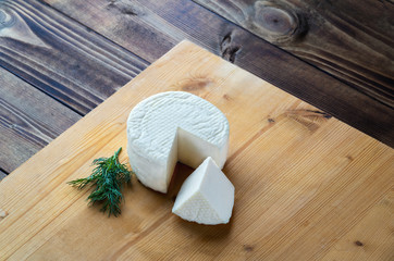 Homemade cheese wheel and greens on wooden board