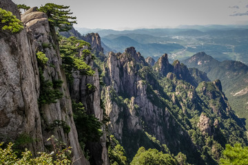 Steep vertical stone on the left leading to a valley and city in the far distance on the right in...