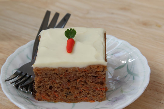 Piece of carrot cake with cream cheese on white plate.