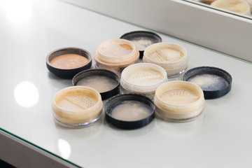 Close-up of makeup  jars filled with loose cosmetic face powder different shades on the white table. 