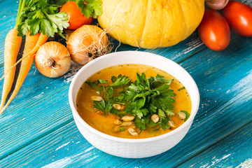 Pumpkin and fresh vegetables soup in white bowl close-up wooden blue background. Natural rustic style. Horizontal frame.