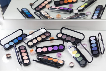 Different color eye shadows palette with reflection in the mirror on makeup artist white table. 