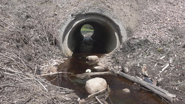 Big culvert under the highway. Before the pipe accumulates a large amount of natural and artificial debris. Before pipe flows the river, where this road debris gets