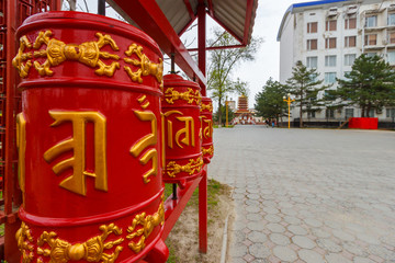 Elista, Kalmykia / Russia - 24 april 2019. Red buddhist prayer wheels on the street of the Elista city with The Government House at the background