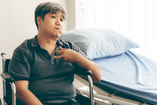 Asian Middle Aged Man  Sitting On A Wheelchair Close To The Patien Bed, His Hands Are Kinking Due To A Nervous System Illness And Paralysis, To Health Care Concept.