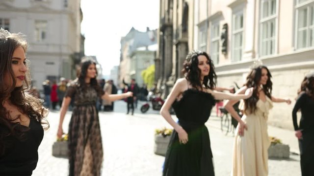 a lot of beautiful, spectacular, girls dressed in exquisite dresses, different colors and crowns, with hairstyles, and great makeup. smiling, dancing in the middle of the street, on a Sunny day