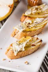 Appetizer bruschetta with pear, honey, walnut and blue cheese on white plate