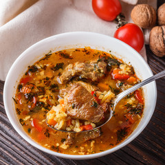 Georgian soup. Kharcho with rice, tomato, beef, garlic and herbs in bowl on wooden table