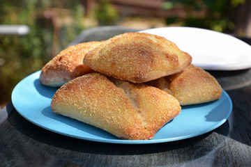 Fresh crusty bread rolls piled up on a blue plate on outdoor table