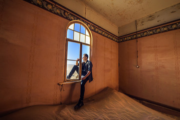 Tourist sits in the window of a room in the ghost town Kolmanskop, Namibia