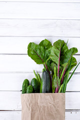 Paper package filled with fresh green vegetables on wooden white background
