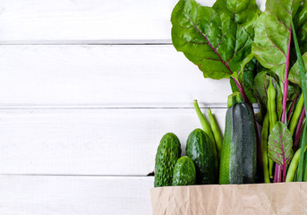 Paper package filled with fresh green vegetables on wooden white background