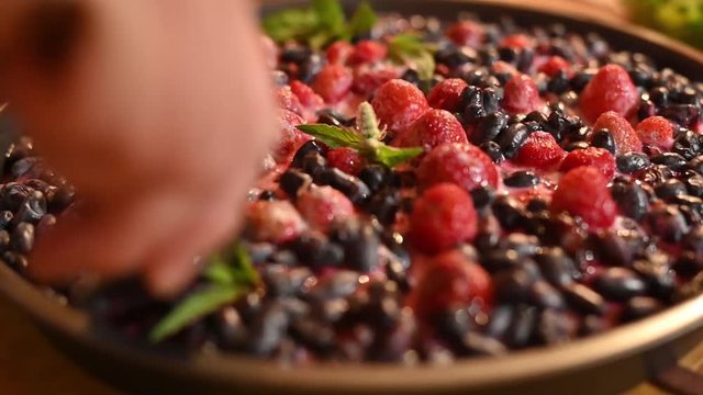 fresh beautiful juicy appetizing berry cake cut with pie shovel. with honeysuckle and strawberry decorated with mint leaves. female hands carefully divided into parts. slow motion close-up