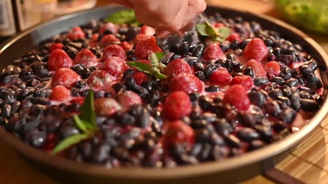 fresh beautiful juicy appetizing berry cake cut with pie shovel. with honeysuckle and strawberry decorated with mint leaves. female hands carefully divided into parts. slow motion close-up