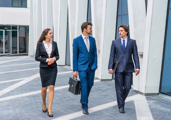 Confident businesspersons talking in front of modern office building. Businessmen and businesswoman have business conversation. Banking and financial market concept.