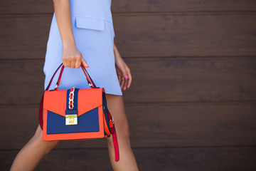 Stylish blue with orange leather women bag. The girl holds in her hand. Young woman walking down...