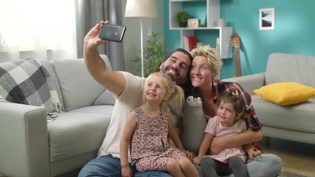 Smiling parents with daughters taking selfie family photo on floor at home
