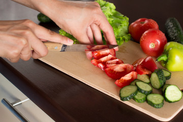 young woman making green salad with cucumber, tomatoes, green pepper, lettuce in a kitchen	