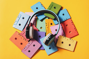 Painted audio cassettes and blue headphones on bright yellow background, copy space, top view. Retro music background