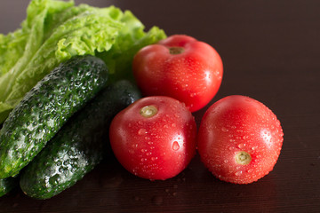 wet tomatoes, lettuce and cucumbers on dark wooden kitchen table	