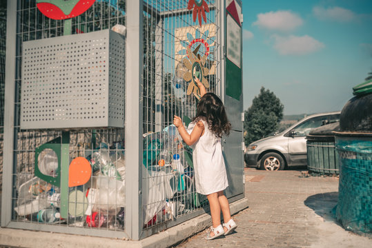 Little Girl Recycling Empty Plastic Water Bottles in Metal Recycling Cage. Child Puts Plastic Waste in Recycling Bins in Street of City.