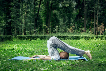 Young handsome white man in sportswear does stretching in the park on the green grass. Prepare a warm-up for yoga or fitness classes.