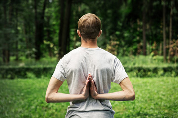 Naklejka na ściany i meble Attractive sporty man doing yoga outdoors in the park. Holding Anjali Mudra behind the back, exercise for flexibility in the hands, wrists.