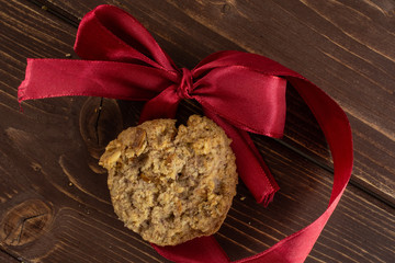 One whole oat crumble biscuit with crimson ribbon flatlay on brown wood