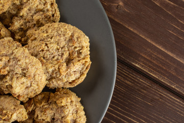 Lot of whole sweet oat crumble biscuit on grey ceramic plate flatlay on brown wood