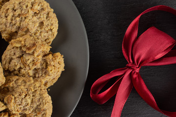 Lot of whole oat crumble biscuit on grey ceramic plate with crimson ribbon flatlay on grey stone